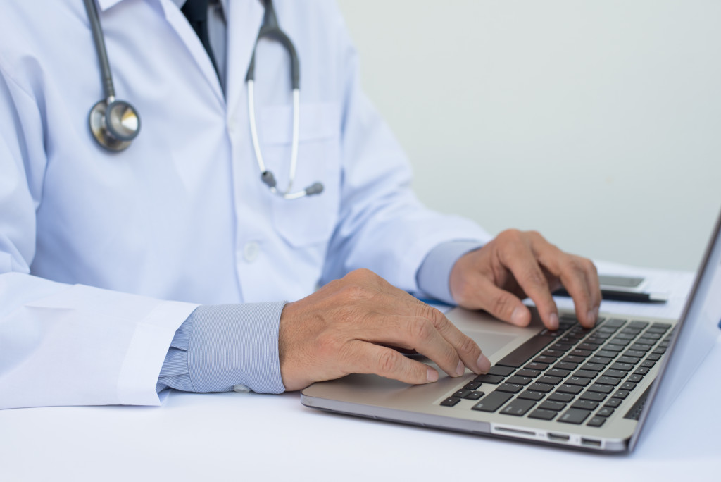 Close up of male doctor working on laptop computer on white desk in hospital, electronic health records system EHRs, teleconference or telemedicine concept.