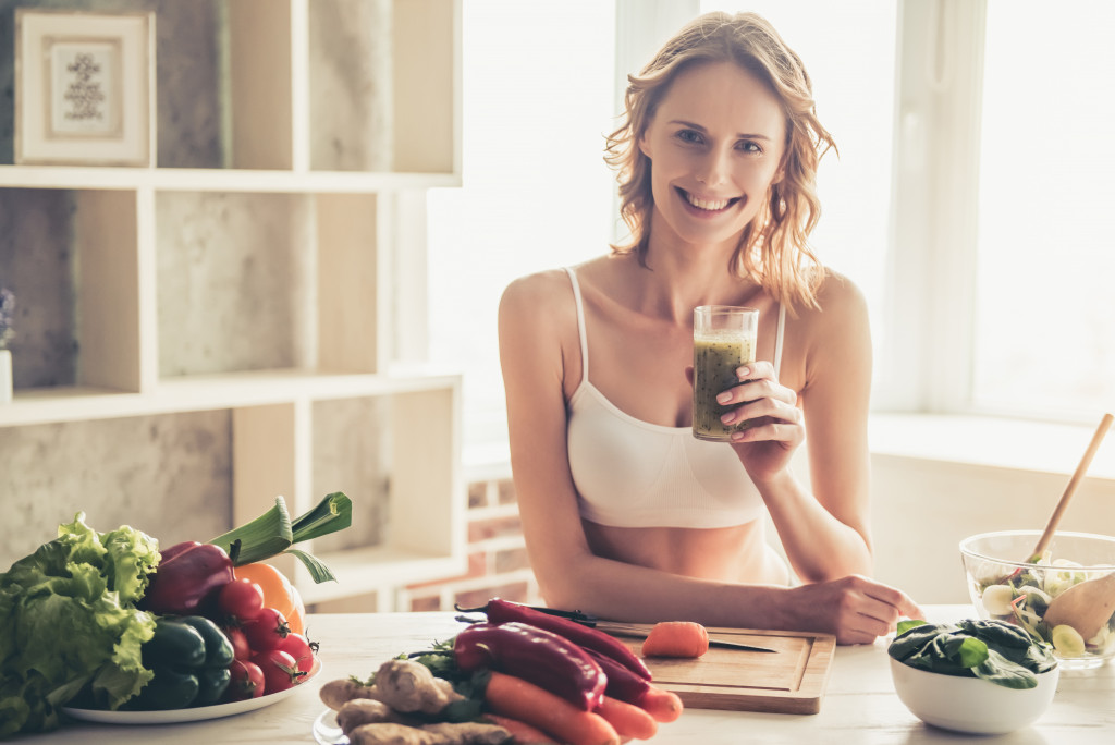 woman drinking healthy drink while fruits and vegetables are arranged in front of her