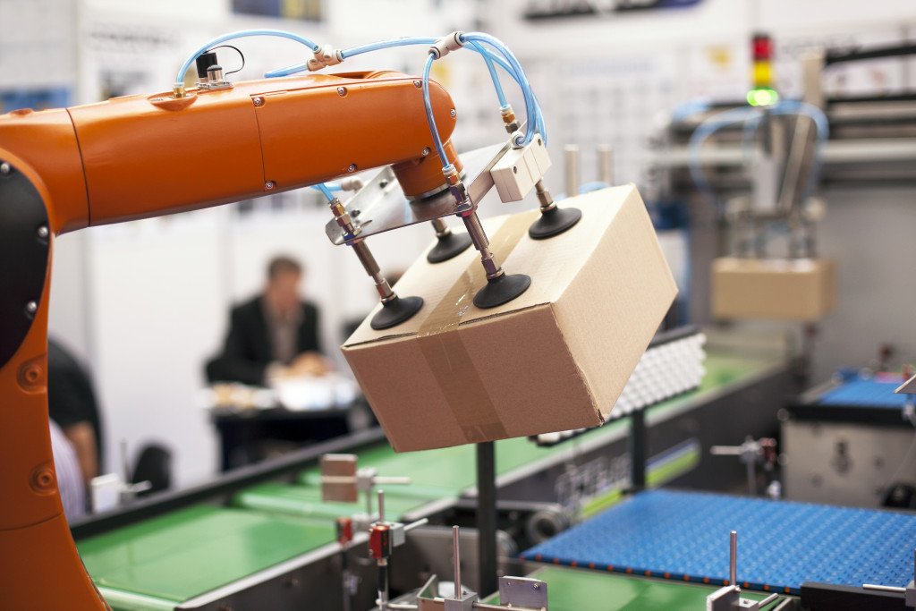 Robot machine with a package in a manufacturing plant factory with workers sitting in background 