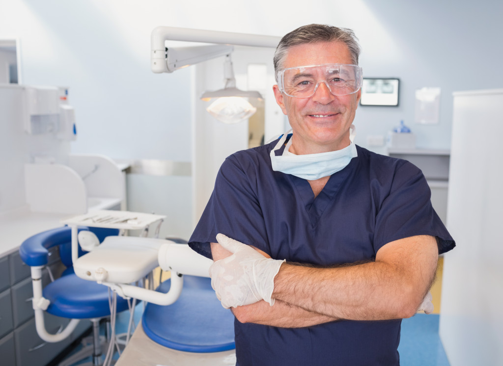 Smiling dentist standing in front of modern equipment in his clinic.