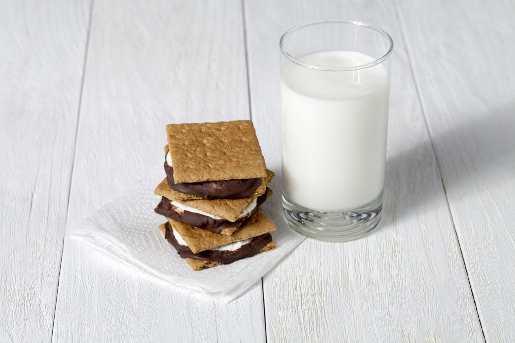 S'mores and a glass of milk on a paper towel over a white wood table 