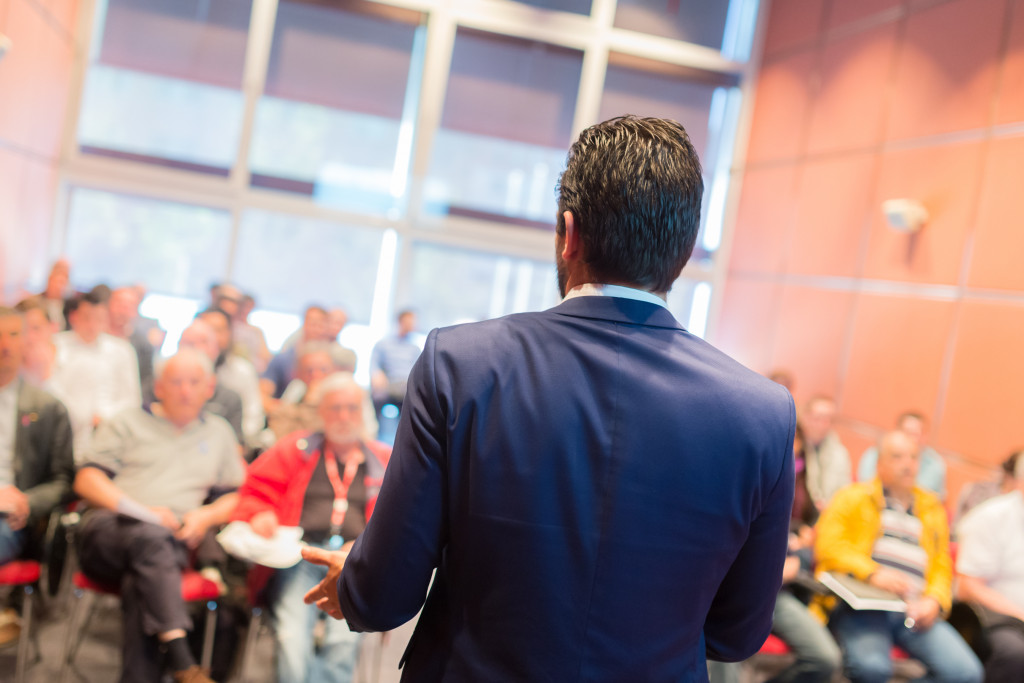 A speaker standing in front of an audience in a conference hall