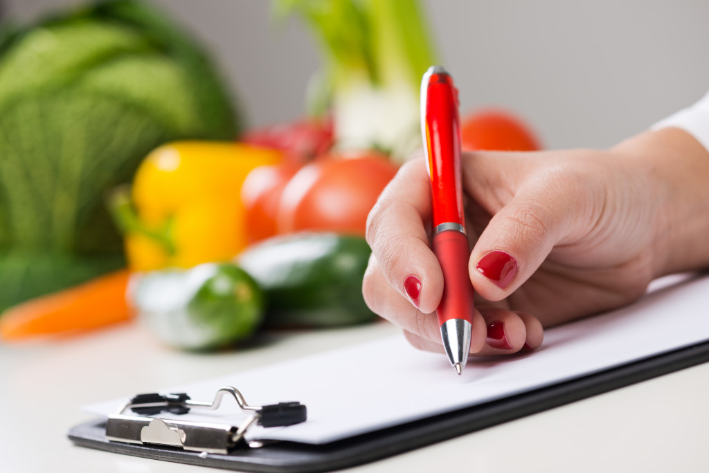 A nutritionist writing on a clipboard with fresh vegetables in the background