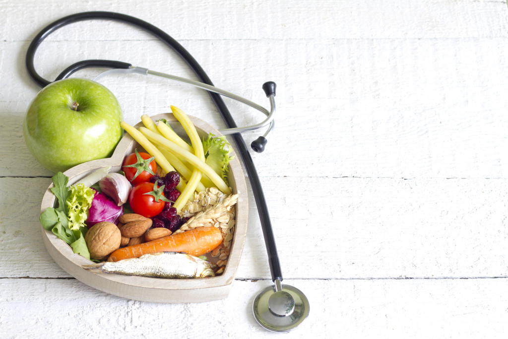 Heart-shaped container filled with healthy food and a stethoscope on the table beside it.
